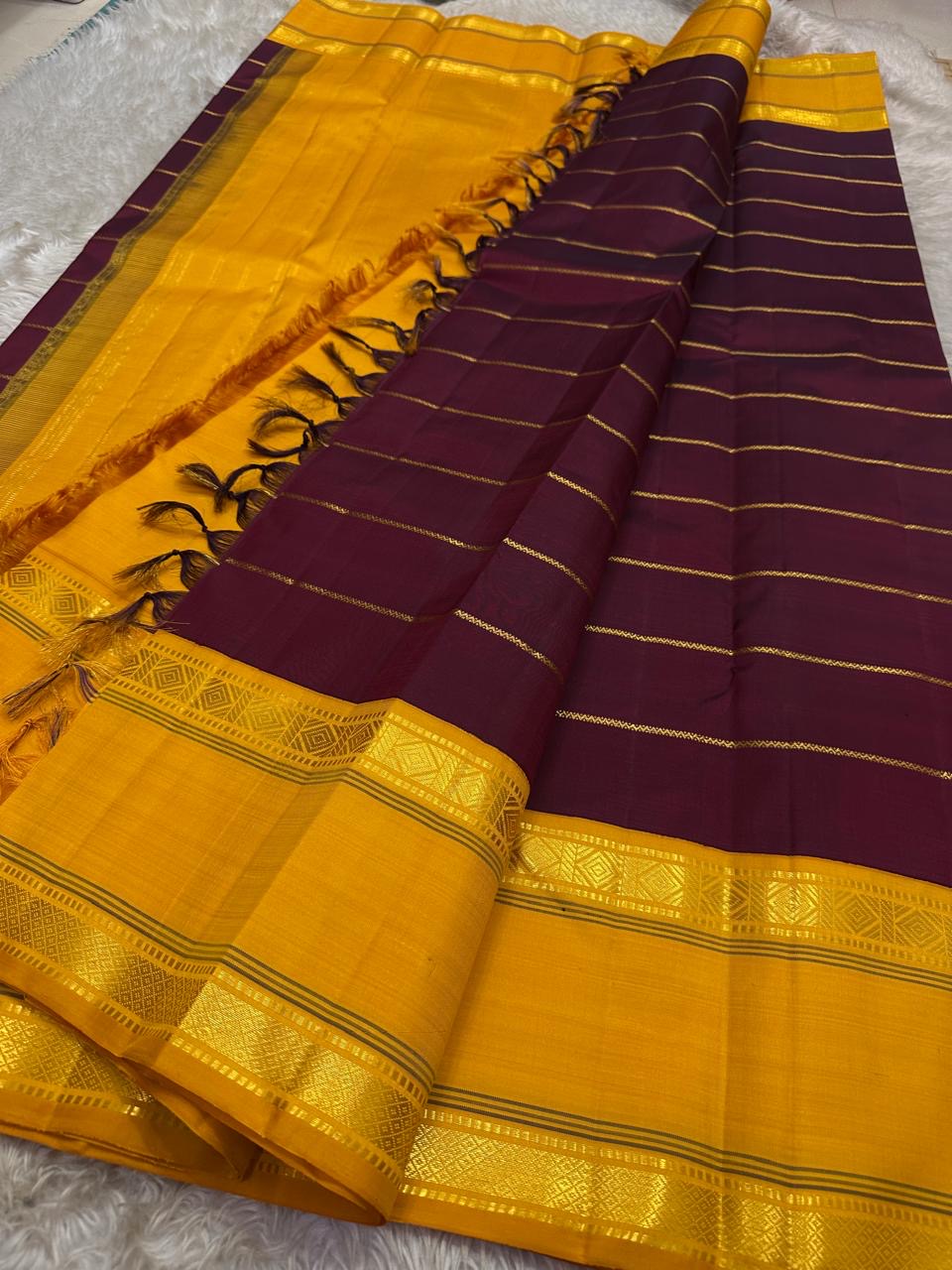 Open drape view of pure Kanchipuram silk saree showing maroon body with mustard zari border and tasselled pallu edge.