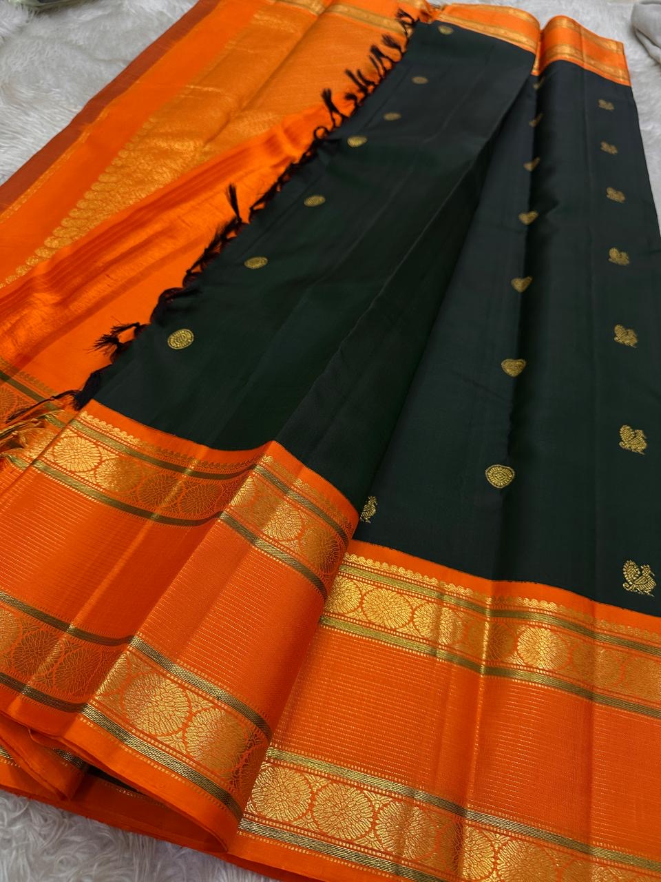 Nirupama ✨ – Bottle-Green Kanchipuram Pure Silk Saree
With Striking Saffron-Orange Korvai Contrast Border rettapet 
Adorned with Gold Rosette Buttas & Medallion Bands
Grand Zari Brocade Pallu in Cascading Motifs