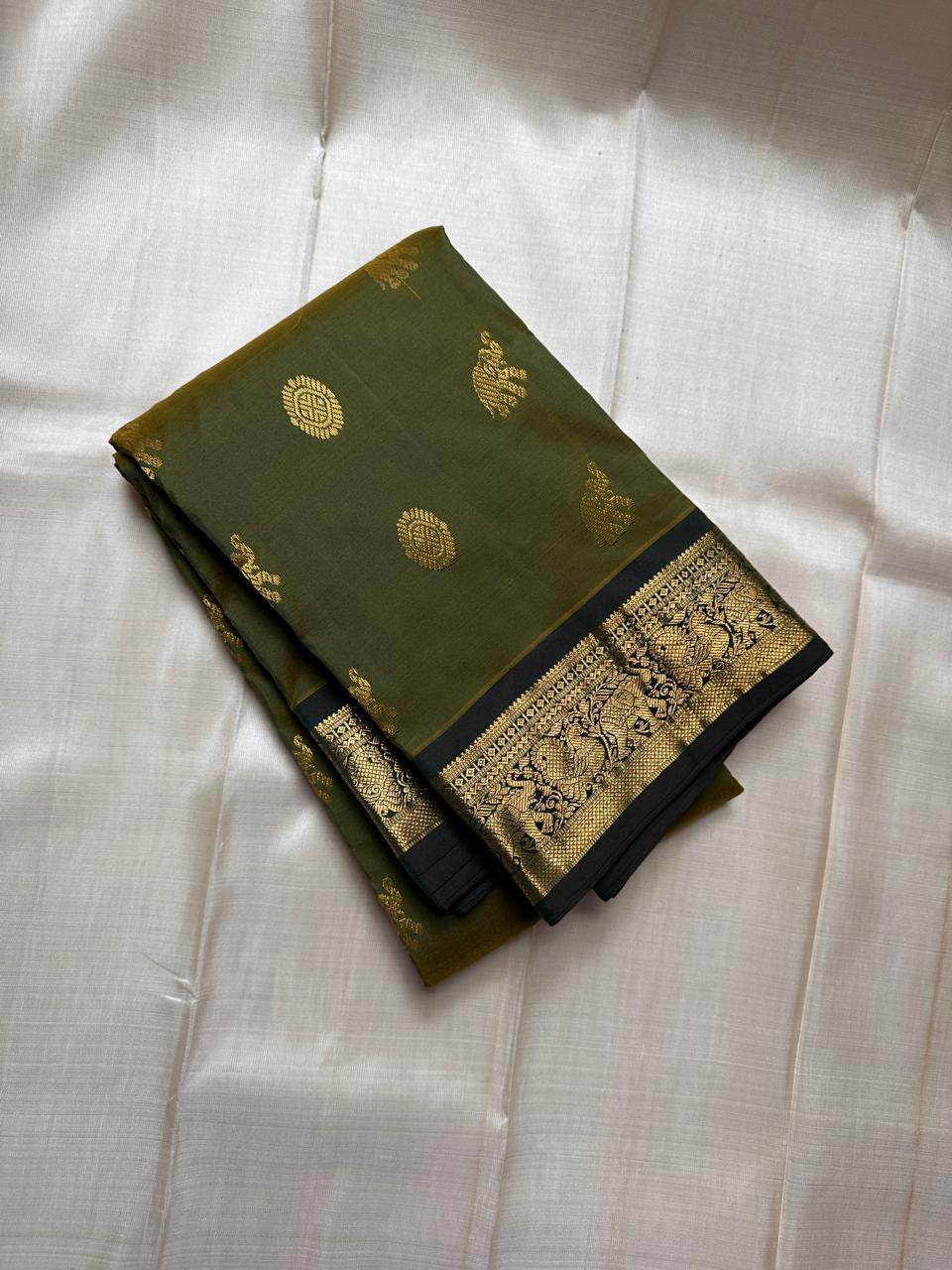 Olive Pachai – Pure Korvai Kanchipuram Silk Saree
Olive green body with gold zari gaja & medallion buttas
Contrast black korvai border with peacock & floral vines
Grand brocade pallu with lattice & temple patterns
Silk Mark Certified …chk description