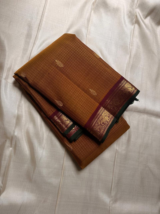 Amber Oosikattam ✨ – Pure Kanchipuram Silk Saree
Burnished Amber-Gold Body in Oosi Zari Kattam with Leaf Buttas
Deep Maroon Korvai Border with Green Selvedge & Elephant Motifs
Regal Maroon Pallu with Intricate Gold Zari Brocade
Silk Mark Certified |