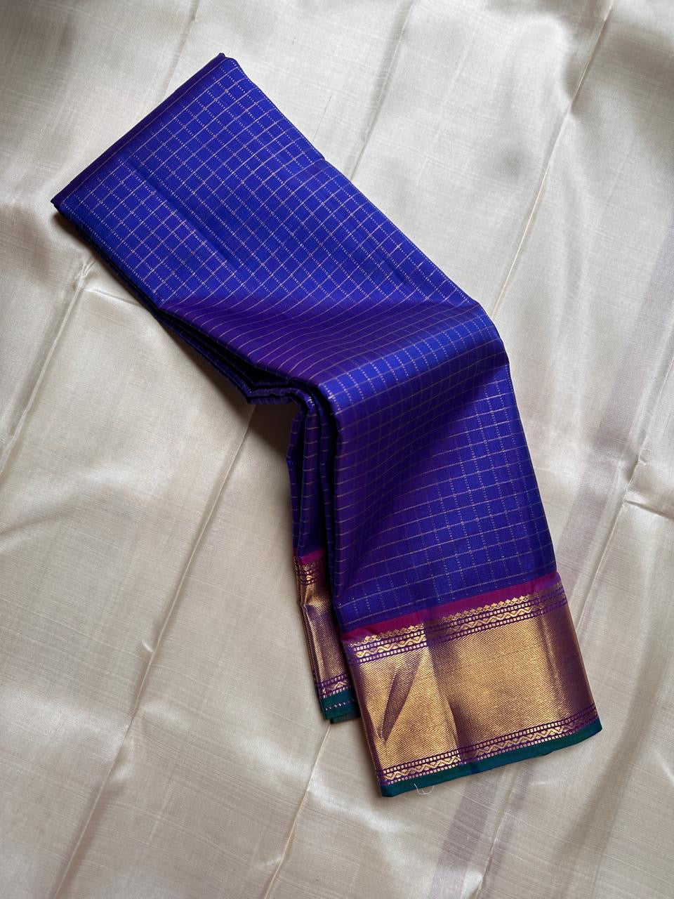 Sapphire Zari Kattam – Pure Kanchipuram Silk Saree
Brilliant Sapphire Blue Body with Gold Zari Checks
Broad Golden Border with Magenta Highlights & Temple Motifs
Royal Magenta Pallu with Lustrous Zari Stripes

Silk Mark Certified, delivery in 2 weeks