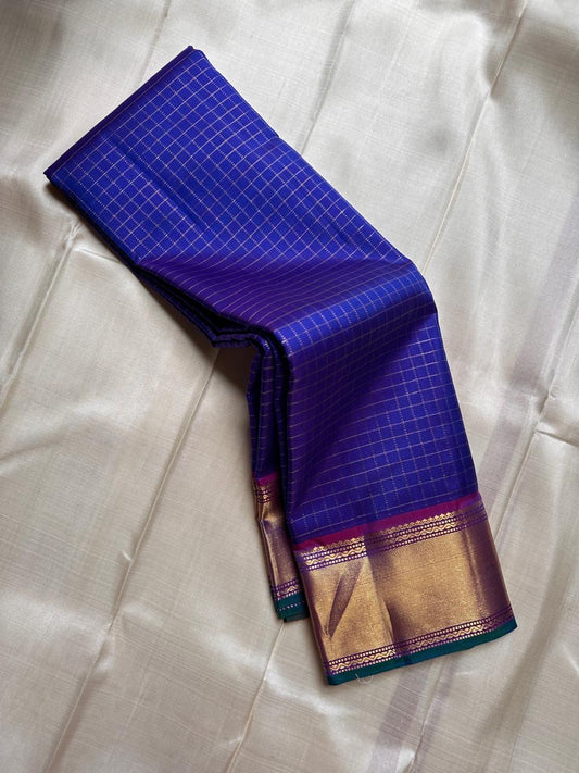 Sapphire Zari Kattam – Pure Kanchipuram Silk Saree
Brilliant Sapphire Blue Body with Gold Zari Checks
Broad Golden Border with Magenta Highlights & Temple Motifs
Royal Magenta Pallu with Lustrous Zari Stripes

Silk Mark Certified, delivery in 2 weeks