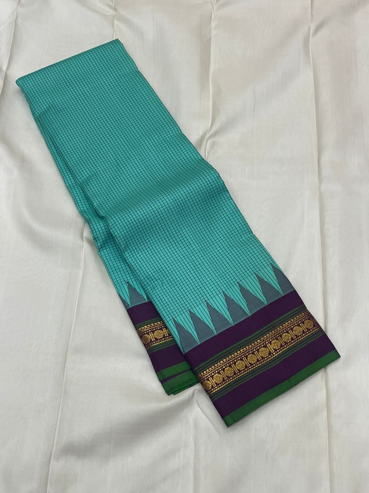 Gopura Neelam — Kanchipuram Pure Silk Saree

 

 

Teal-green body with micro kattam checks for a sleek drape

Regal aubergine korvai border with gopuram/temple motifs & gold zari

Parrot-green selvedge for a fresh, festive pop of contrast

Aubergine pall