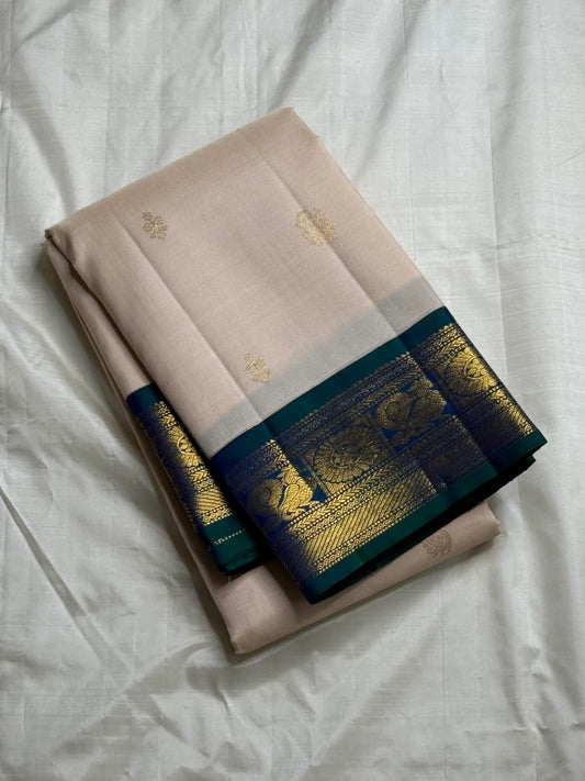 Mayilkazhuthu Shwetham — Pure Kanchipuram Silk Saree
Soft Ivory-Blush Body with Gold Zari Buttas & Peacock Blue-Green Border
Silk Mark Certified • Free Shipping within USA • Ships in Two Weeks