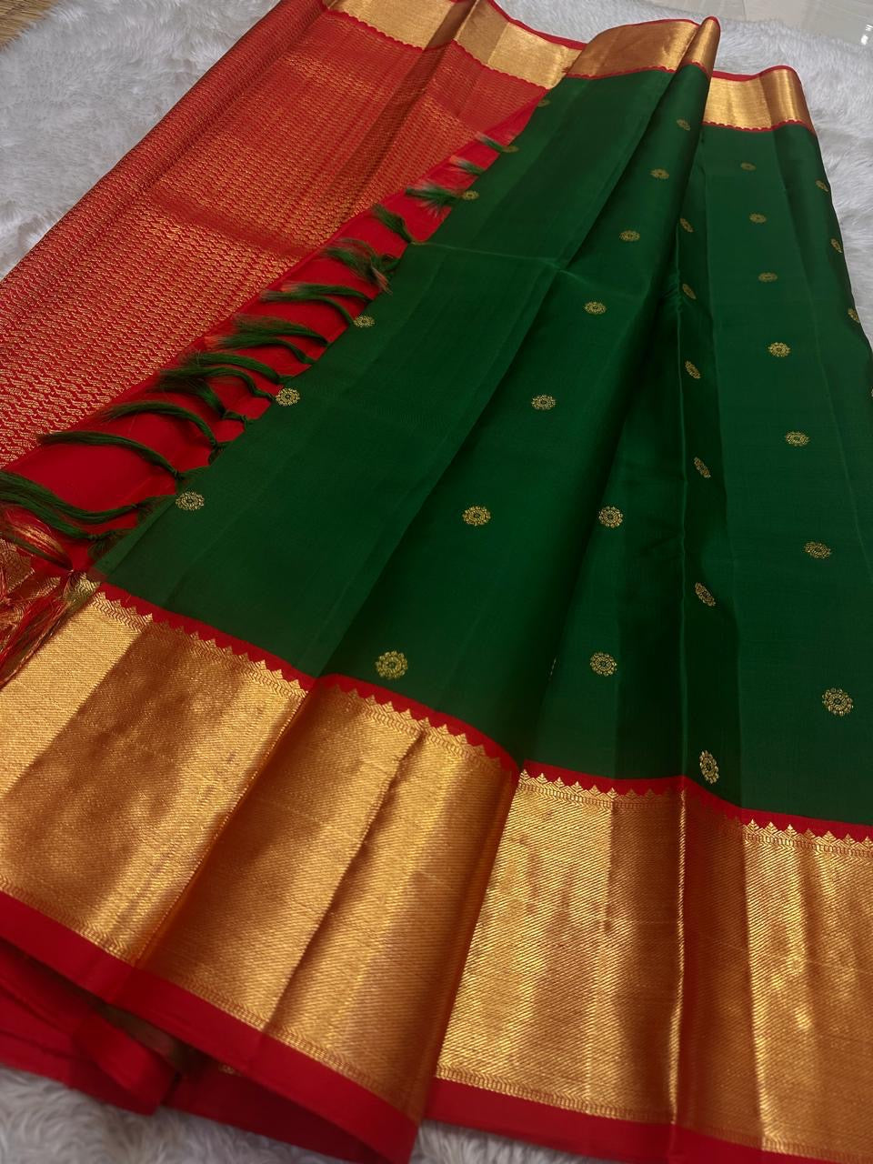 Close view of emerald green silk body with small gold zari buttas and contrast red border