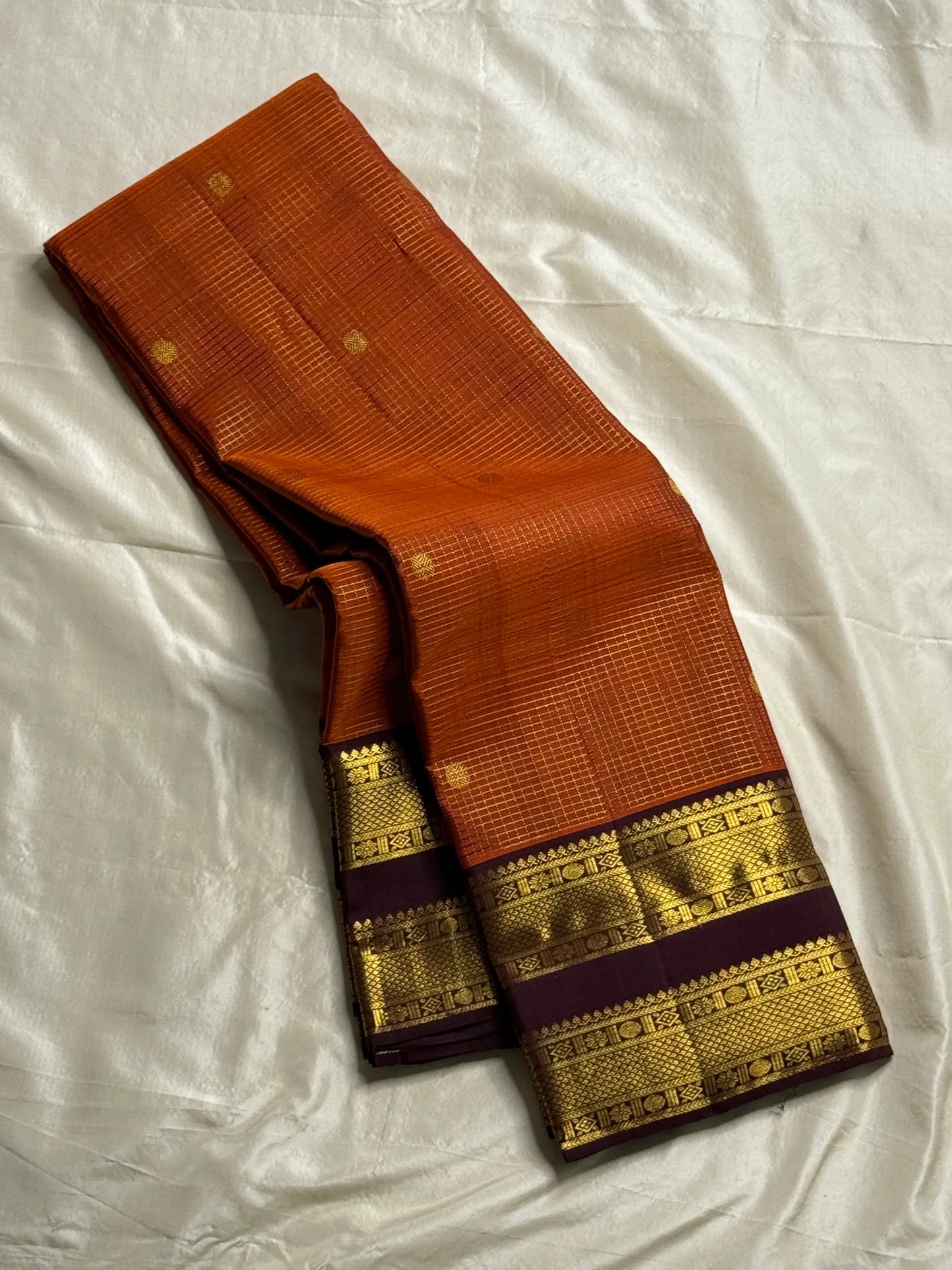 Rust Orange Kattam Rettapet – Pure Silk Kanchipuram Saree
Rust Orange Body with Petite Gold Buttas & Fine Kattam Grid
Deep Aubergine Rettapet Korvai Double-Line Contrast Border
Rich Zari Diamond & Chevron Brocade Pallu
Comes with Contrast Aubergine Blouse