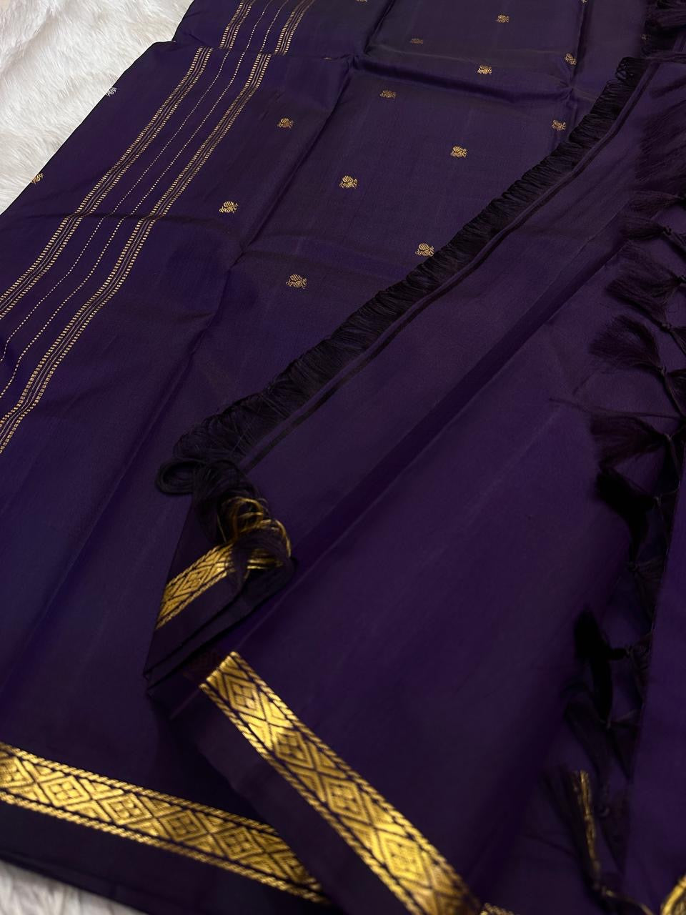 Close-up of purple Kanchipuram silk saree pallu showing rows of gold zari lines, tassels, and narrow diamond-pattern border.