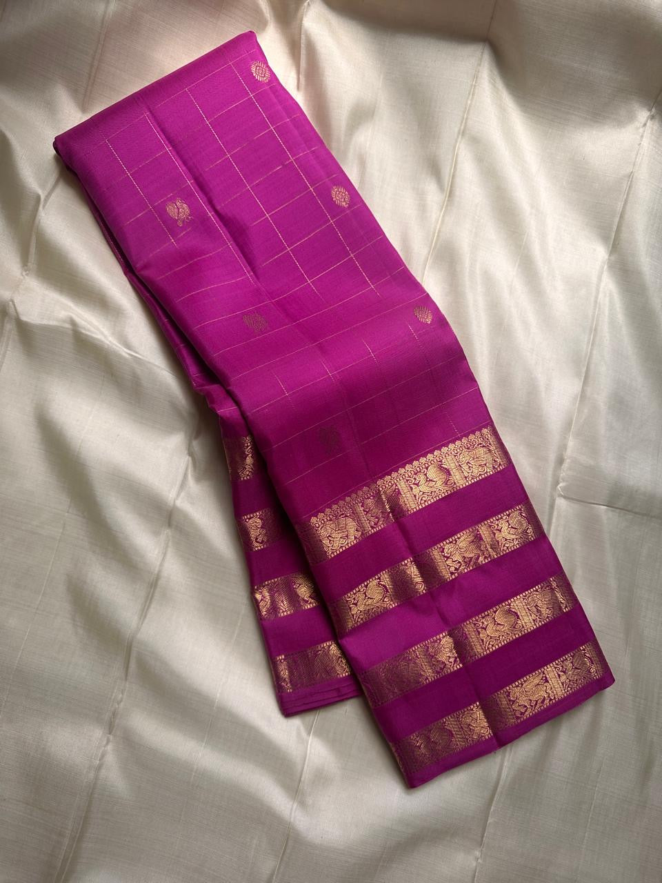 vasantham  Fuchsia pink – Handwoven Kanchipuram Silk Saree A poem in Fuchsia silk. The body glows in a serene vibrant Fuchsia, softly accented by delicate gold vertical lines and dainty gold zari buttas that glint like little blessings.