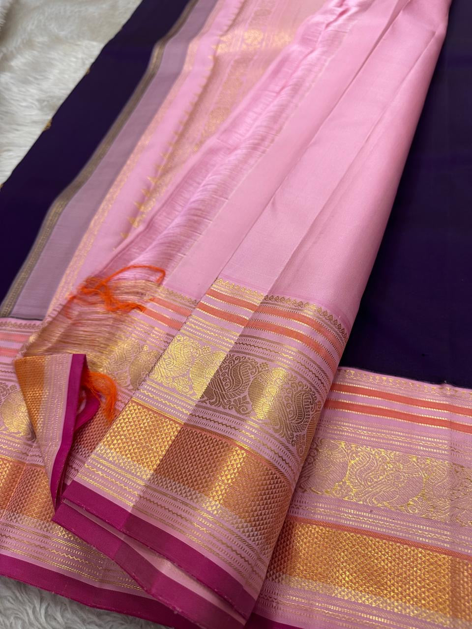 Shyamala—named after the deep, dark shade it embodies 💜 A pure Kanchipuram silk masterpiece with a rich purple body sprinkled with golden zari buttas. The contrast pink border glows with floral and paisley zari motifs, accented in coral and rose-gold, wh