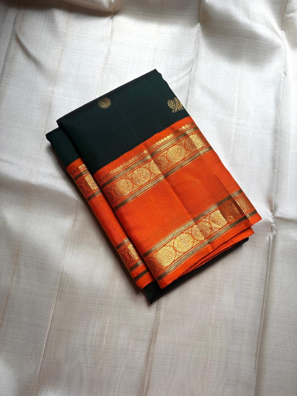 Nirupama ✨ – Bottle-Green Kanchipuram Pure Silk Saree
With Striking Saffron-Orange Korvai Contrast Border rettapet 
Adorned with Gold Rosette Buttas & Medallion Bands
Grand Zari Brocade Pallu in Cascading Motifs