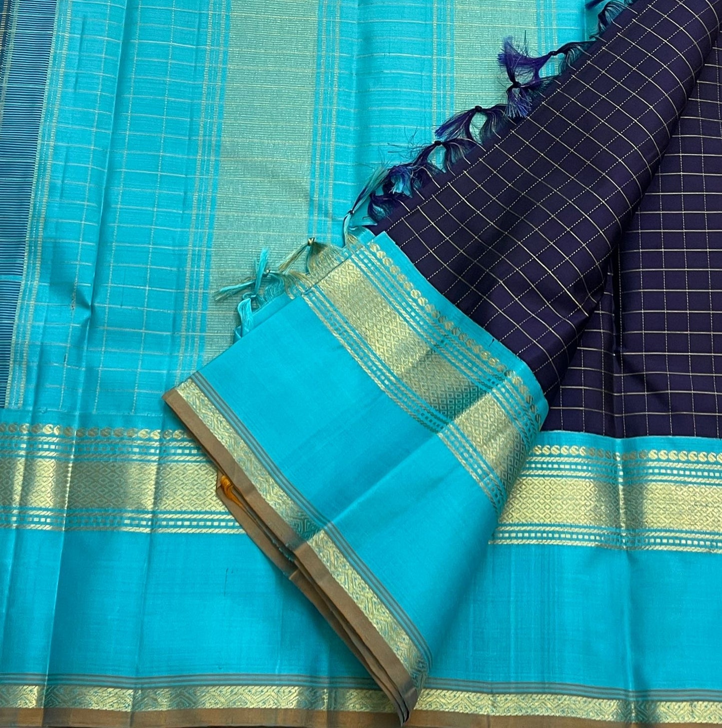 Indigo Teal Kattam – Pure Silk Kanchipuram Saree
Deep Indigo Body with zari Kattam Checks
Teal Contrast Korvai Border with maanga pet and mayil kann border, maanthulir selvedge  , silk mark certified -ships in two weeks