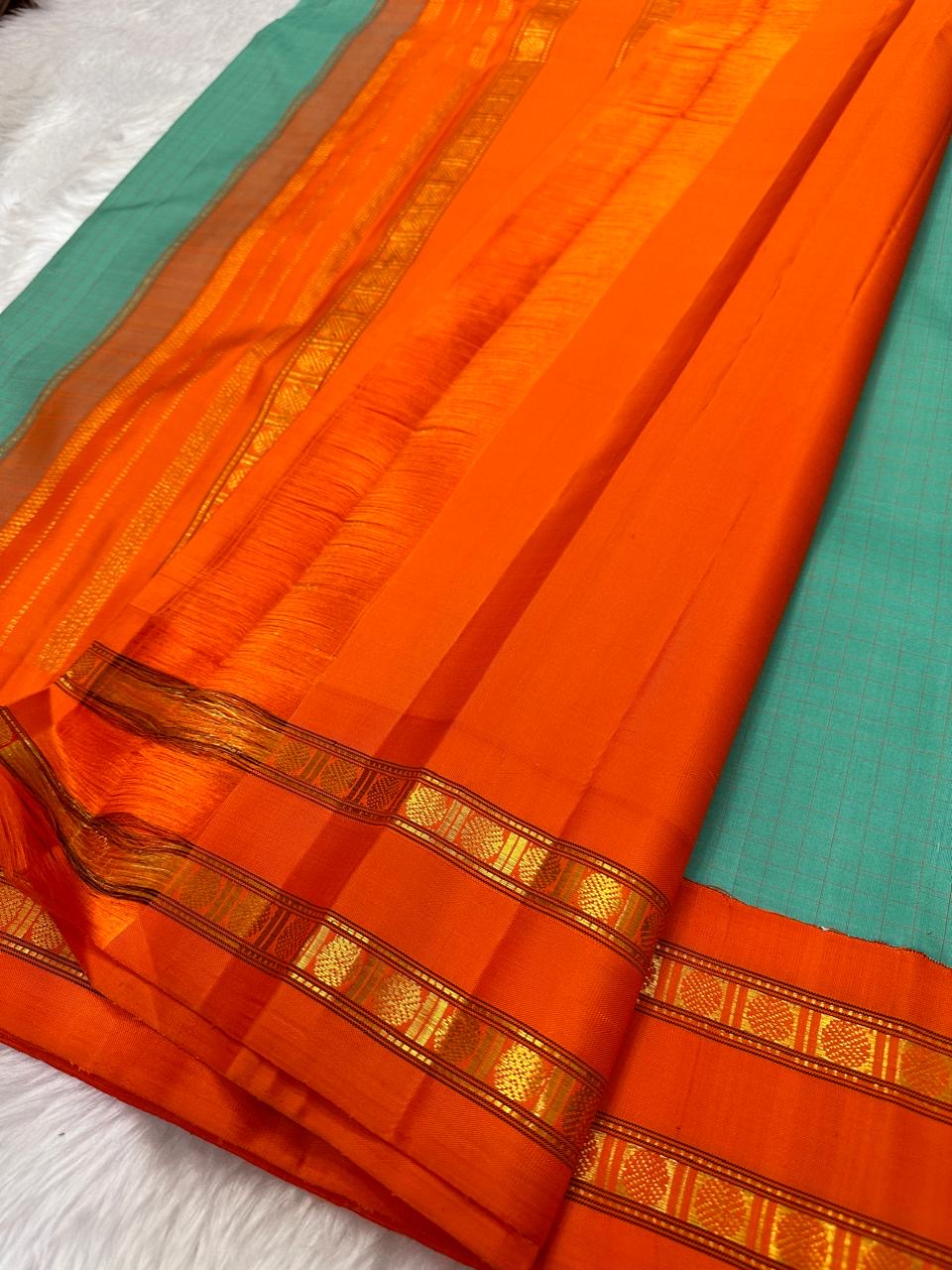 Sharvani blue sea green – sea green  Checked Silk Saree with an Orange red  shot color Zari Border & Vibrant Pallu A timeless silk saree featuring a cream body with delicate red checks, complemented by a striking churan orange  zari border pallu.