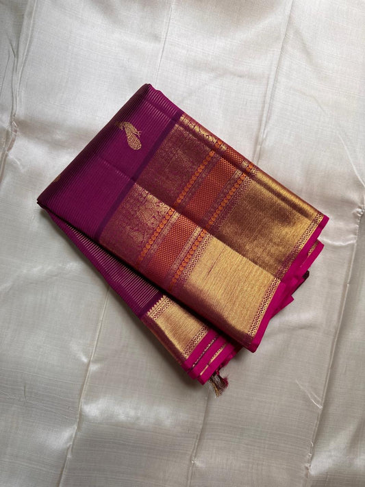 Magenta pinstriped Kanchipuram silk saree with scattered peacock buttas and wide gold zari border, draped on ivory silk