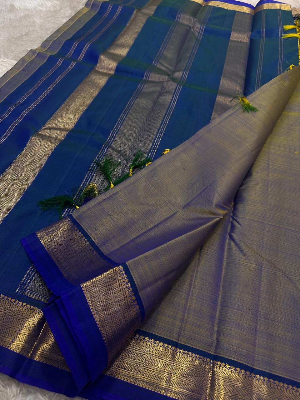 Varnam – Dove Tail Gray & Peacock Blue Kanchipuram Silk Saree. Featuring rich gold paisley buttas, a bold chevron zari border, and pure handloom silk craftsmanship ✨ Silk Mark Certified | Blouse Stitching Available | Free USA Shipping