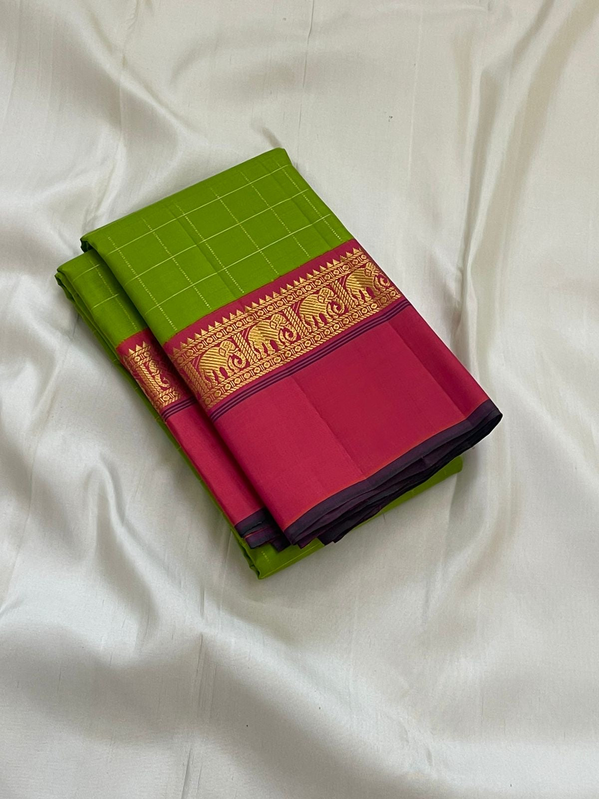 Valli Pachai – Kanchipuram Pure Silk Saree

Parrot-green body in kattam (grid) checks with subtle zari lines

Korvai contrast rani-pink borders featuring gaja (elephant) procession & temple reku motifs

Rich rani-pink zari pallu with vertical bands