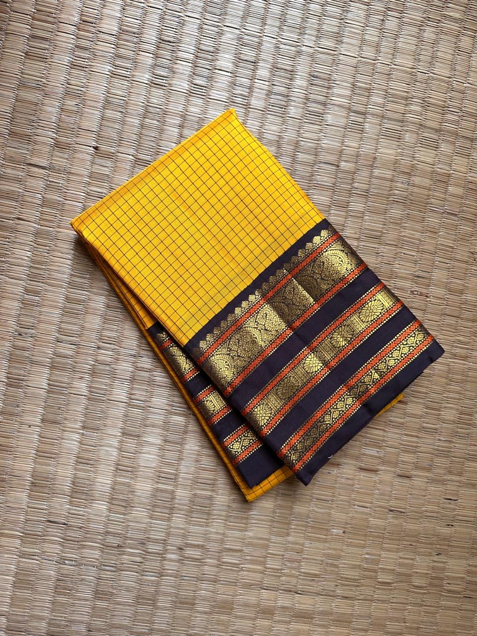 Yellow kattam-check Kanchipuram silk saree with contrast black pallu and gold zari border, fully opened.