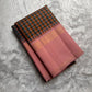 Nirai – A Madras-Inspired Kanchipuram Silk in Amber & Pastel Pink.
Woven with fine podi kattam checks in black, amber orange, and grey.
The pastel pink border with pillayar moggu detailing adds softness, with a  seer zari pallu