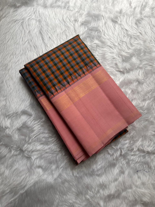 Nirai – A Madras-Inspired Kanchipuram Silk in Amber & Pastel Pink.
Woven with fine podi kattam checks in black, amber orange, and grey.
The pastel pink border with pillayar moggu detailing adds softness, with a  seer zari pallu