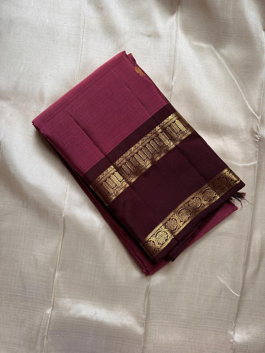 Folded maroon Kanchipuram silk saree with contrast coffee border and gold zari woven detailing