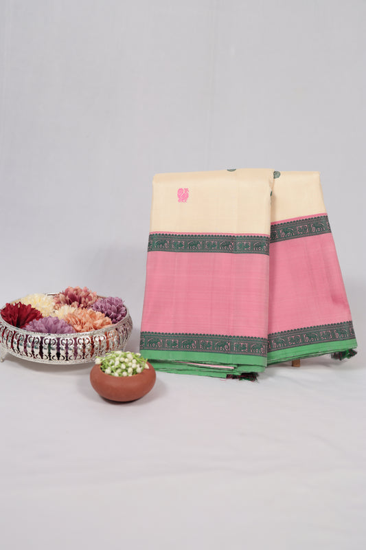 Folded ivory and lotus pink no-zari Kanchipuram silk saree with green silk-thread border, styled with flowers and jasmine on a white backdrop