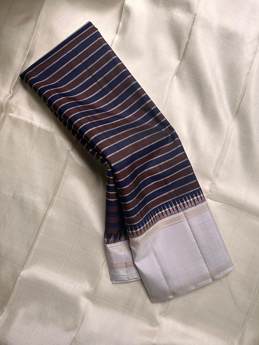 The most unique striped pure silk Kanchipuram with the faintest dove grey border with thazampoo reku , a body of navy and coffee brown stripes separated by distinct zari work ! Truly stunning and rare
