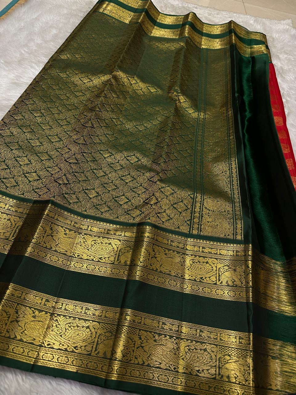 Folded saree showing red body with gold buttas and wide green zari woven elephant border