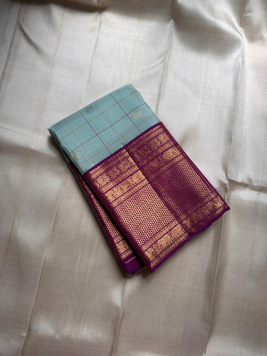 Shanti Blue – Pure Kanchipuram Silk Saree
Pleasant Blue Body with Purple Grid Checks & Zari Buttas
Deep Purple Korvai Border with Elephant & Floral Motifs
Majestic Zari-Dense Pallu in Traditional Weaving
Coordinated Blouse in Blue with Elegant Zari Border