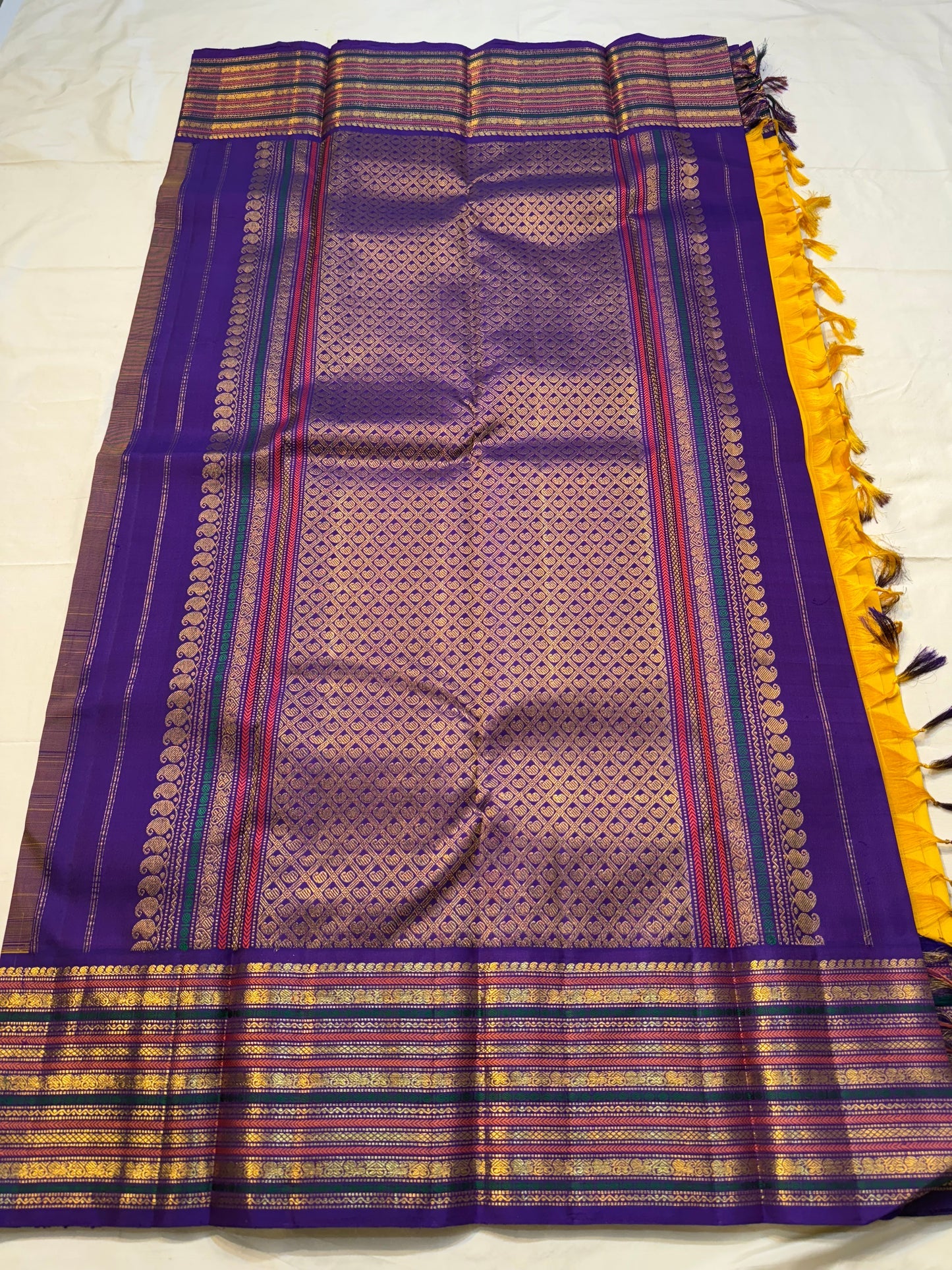 Swarna Kanakam Mayil Chakram — Pure Kanchipuram Silk Saree
Radiant turmeric-gold body adorned with silk-thread mayil and chakram buttas, framed by a regal vadamalli zari-woven korvai border and rich purple pallu.
Silk Mark Certified • Blouse Stitching Ava