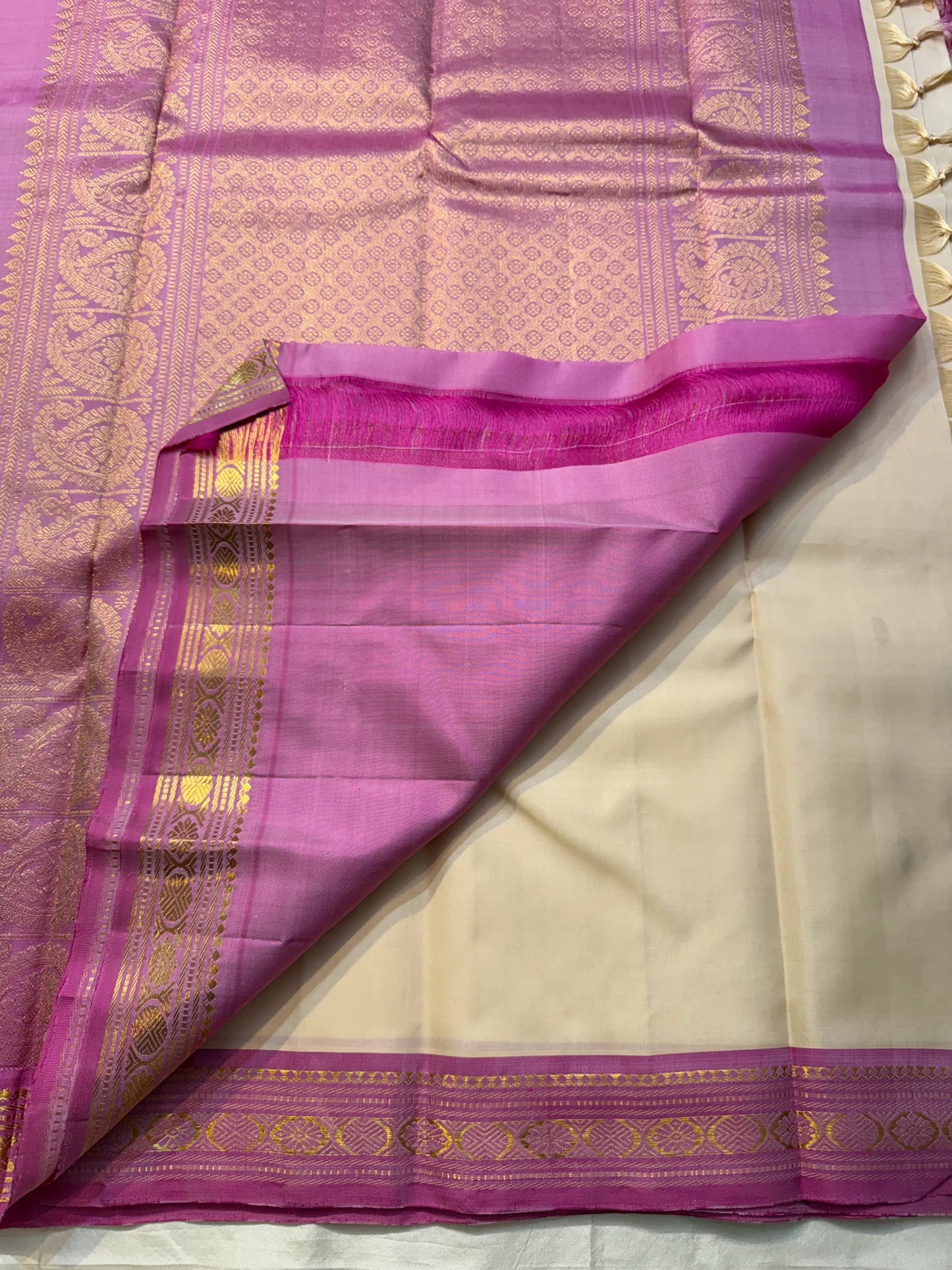 Close view of saree pallu in magenta-lavender with dense gold zari woven pattern, beside the cream body and border.