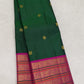 Folded deep emerald-green Kanchipuram silk saree with scattered gold zari buttas and a vivid magenta Varisaipet border.