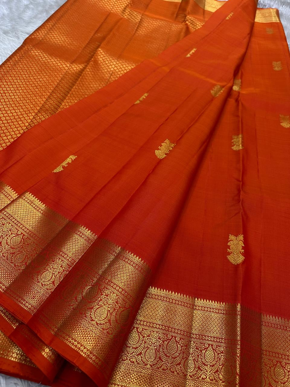 Close-up of red Kanchipuram silk saree with dense gold zari weaving along the border and body.