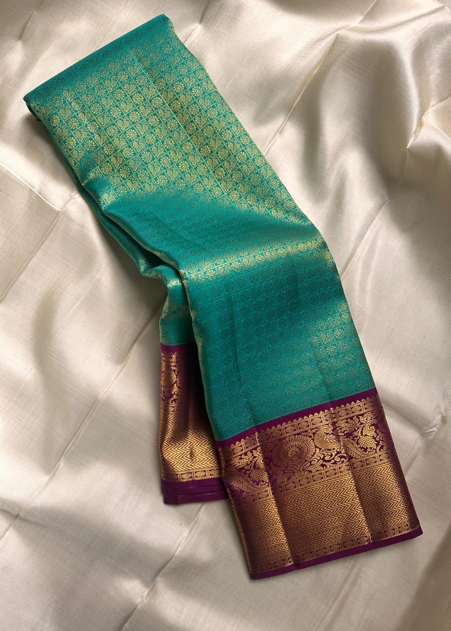 Sindhu- Teal & Purple Kanchipuram Pure Silk Saree with Floral Jaal & Mayil Border
A rich teal base adorned with delicate floral jaal and regal purple mayil borders creates timeless elegance. The diamond-motif pallu adds a bold, sophisticated finish to th
