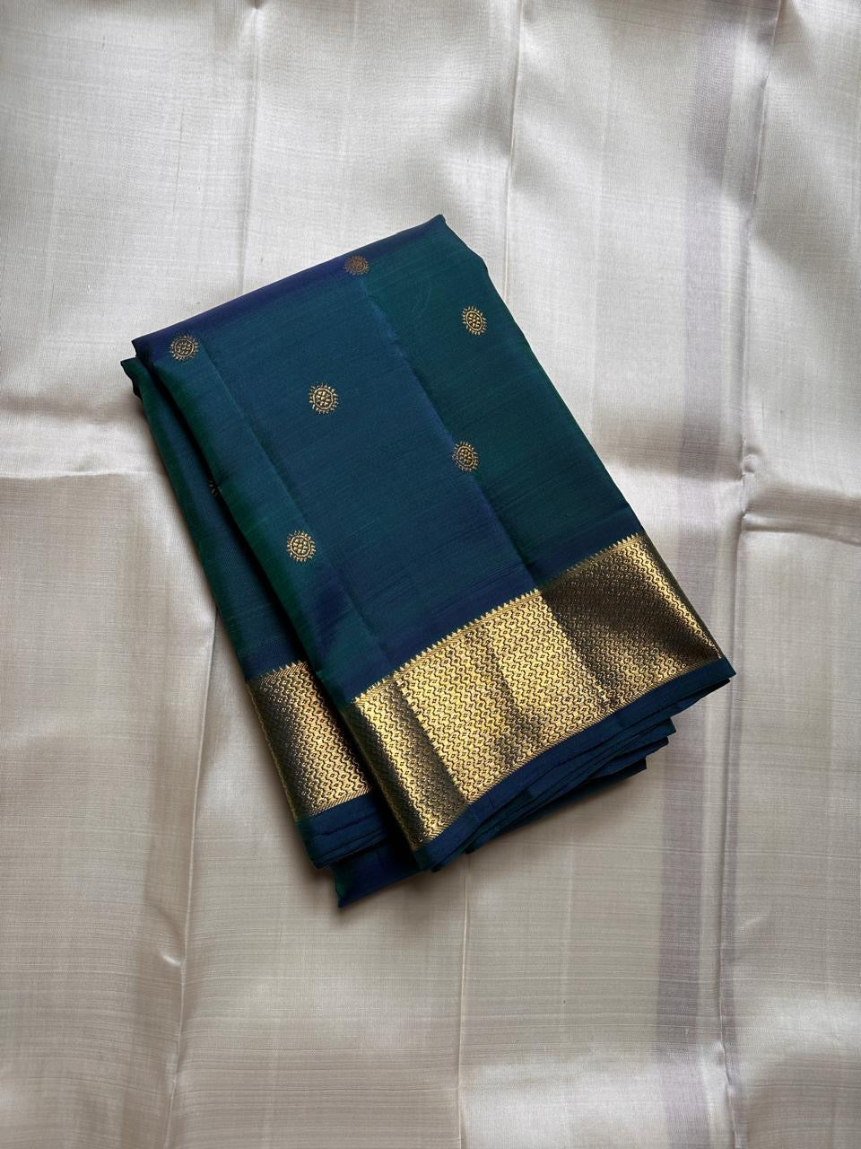 Folded peacock teal Kanchipuram silk saree with gold zari buttas and wide zari woven border