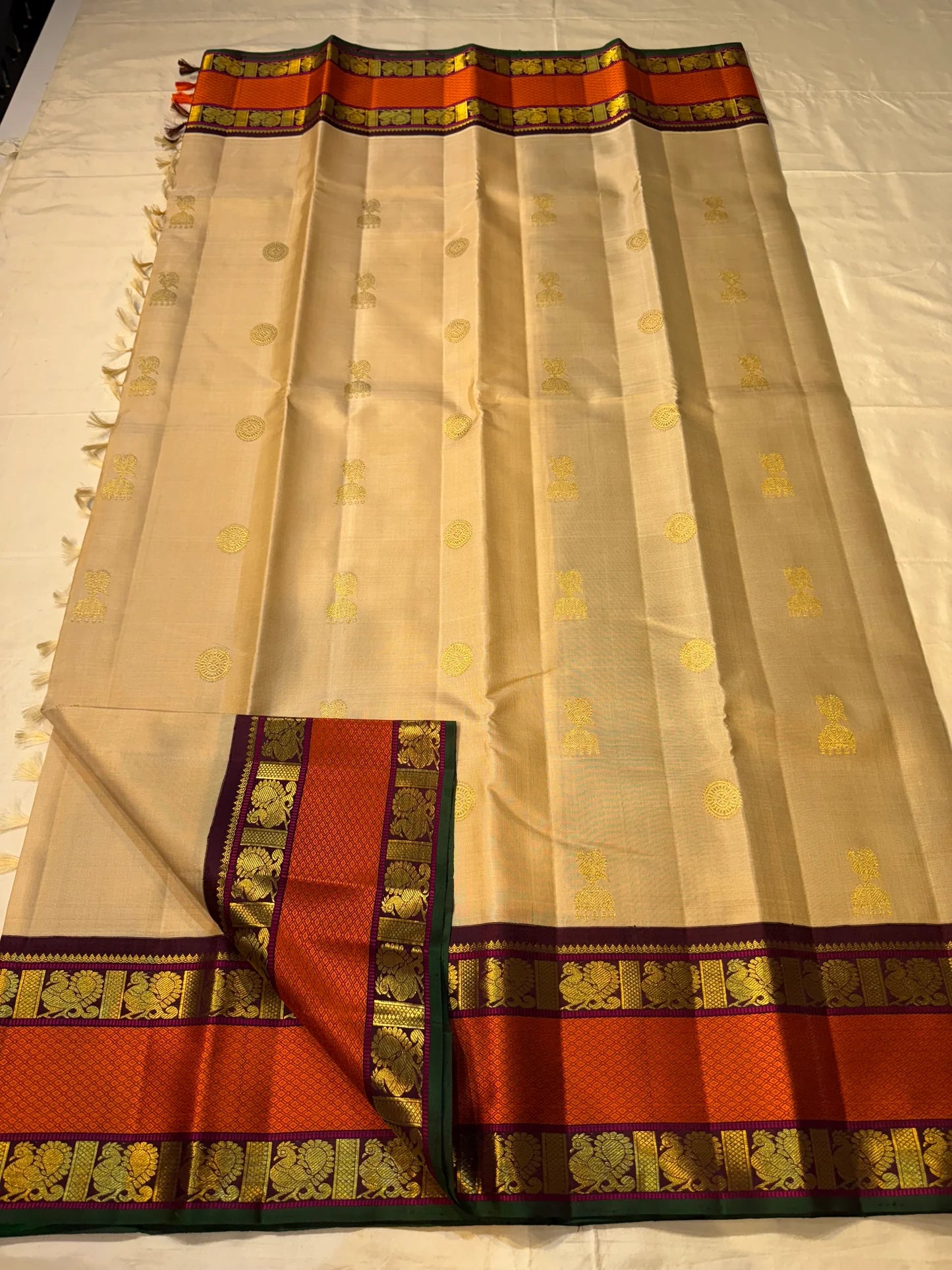 Flat-lay pure Kanchipuram silk saree in biscuit beige with scattered gold buttas and rust orange zari woven border, shipped from New Jersey USA