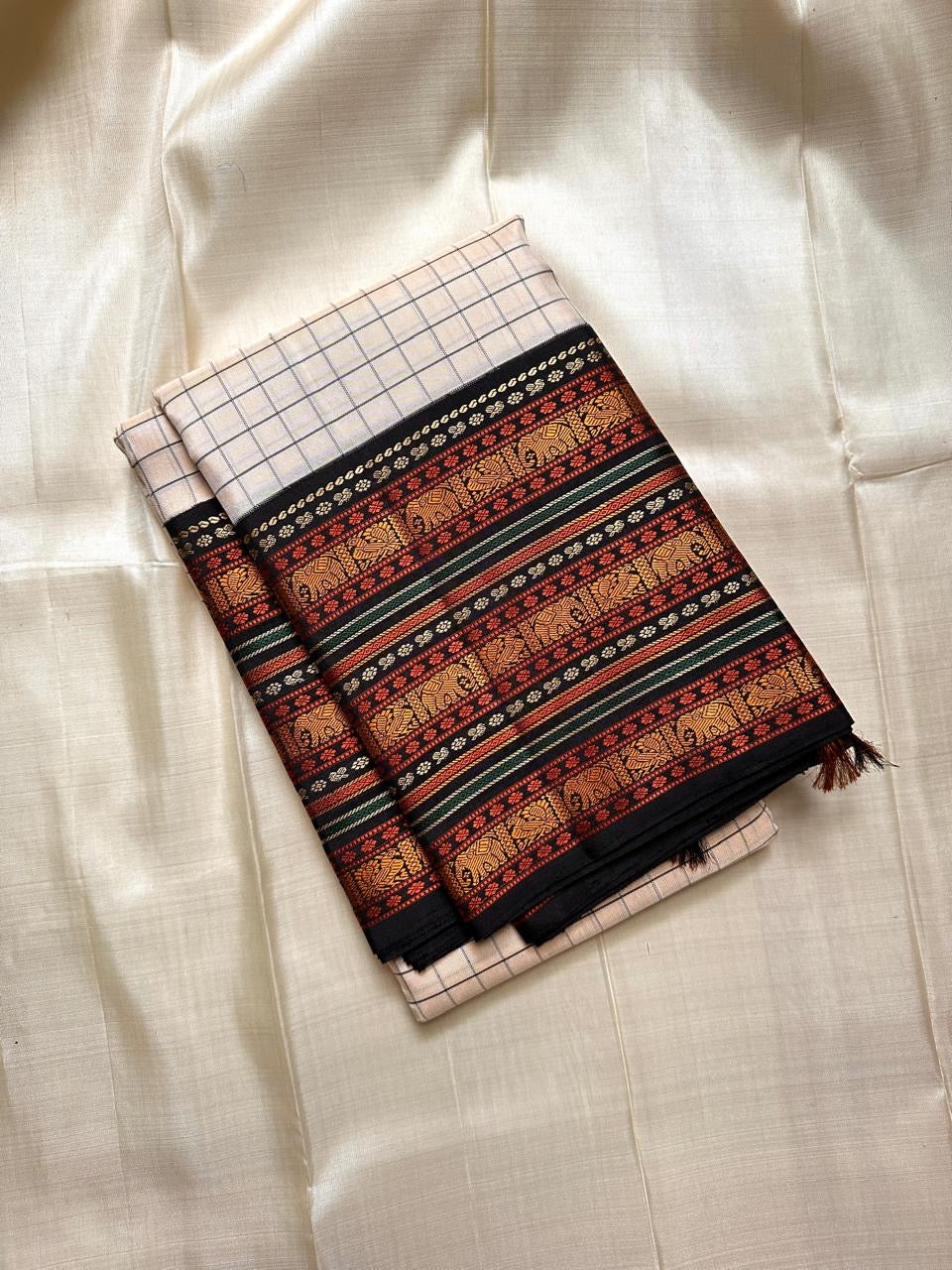Ivory Varisaipet – Pure Kanchipuram Silk Saree
Pattunool Kattam Checks on Ivory Base
Black Borders with Elephant & Floral Motifs
Antique Gold, Rust & Bottle-Green Stripes

Silk Mark Certified, delivery in 2 weeks
