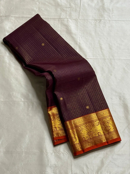 Deep Plum Orange
A regal dance of plum and burnt orange
Micro-checks kissed with golden buttas
Elephant borders marching in heritage grandeur
Brocade pallu glowing in timeless zari brilliance

Silk Mark Certified, delivery in 2 weeks
