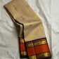 Biscuit beige pure Kanchipuram silk saree draped to show gold buttas and wide rust orange zari woven border with maroon detailing and green selvedge