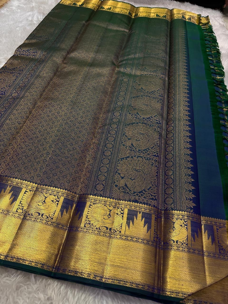 A celestial blend of blue and green, this Kanjivaram silk saree ,adorned with Gandaberunda and Kamalam buttas, golden checks, and a majestic thazhampoo Mayil  border. Zari kattam