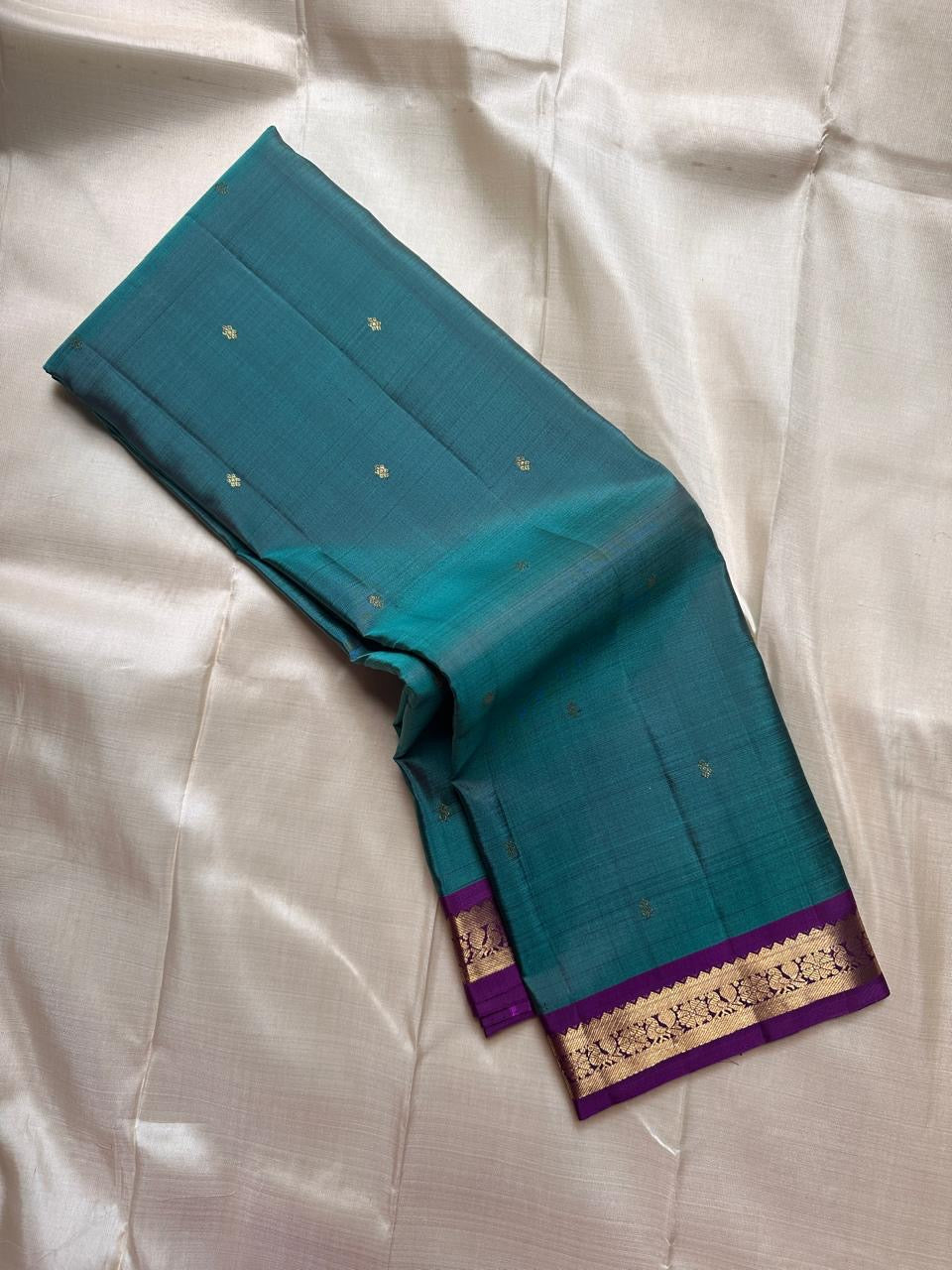 Teal pure Kanchipuram silk saree with small gold butti and a purple zari woven floral border.
