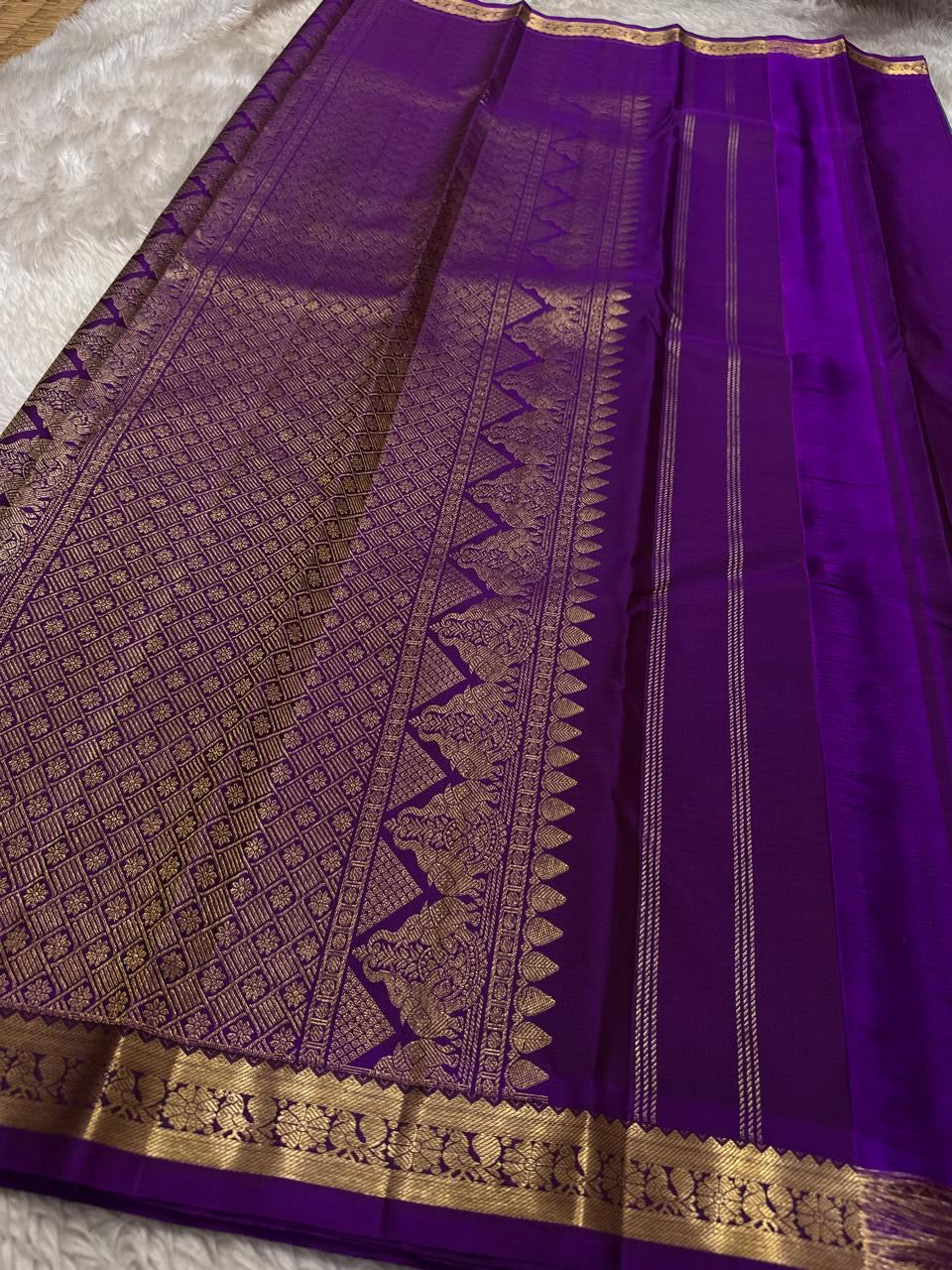 Stack of folded pure Kanchipuram silk sarees in multiple colors, including a teal saree with purple zari woven border.