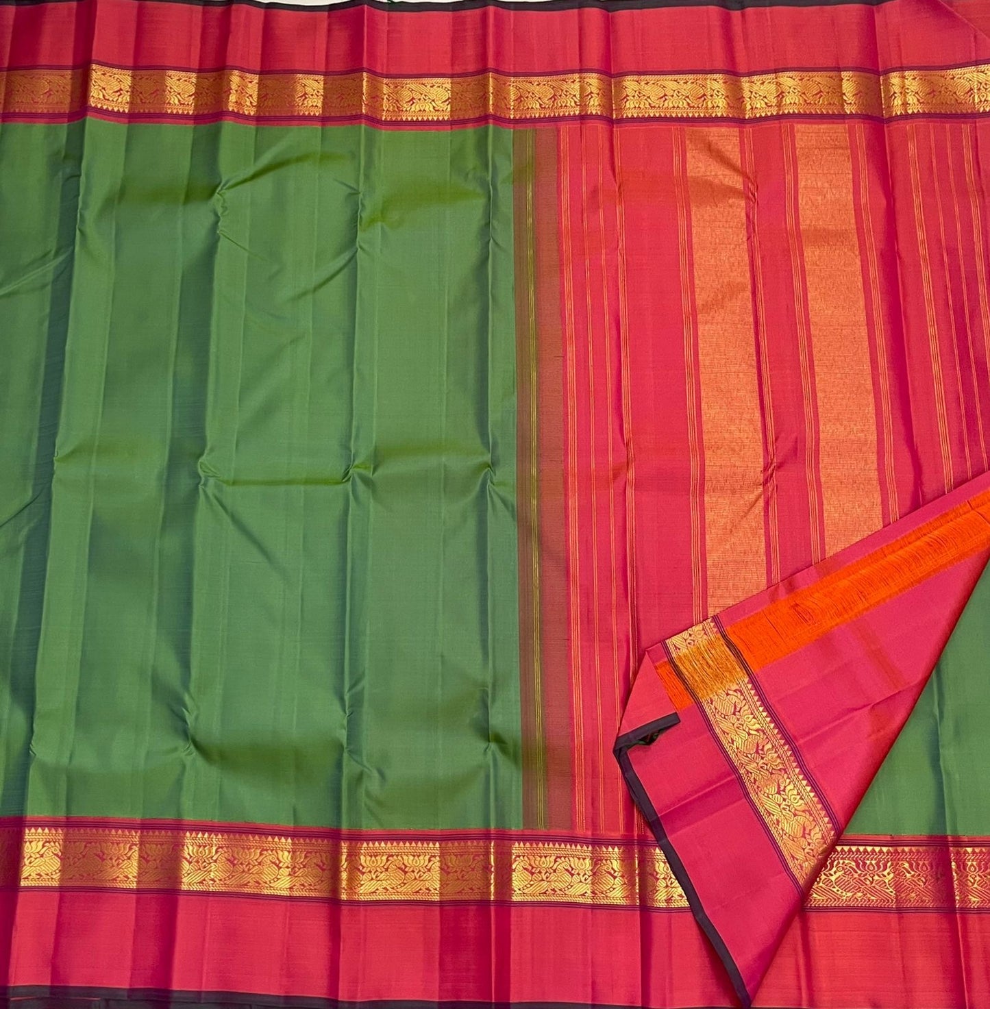 Full view of green saree body with pink border and gold zari woven band, alongside a pink striped pallu section.