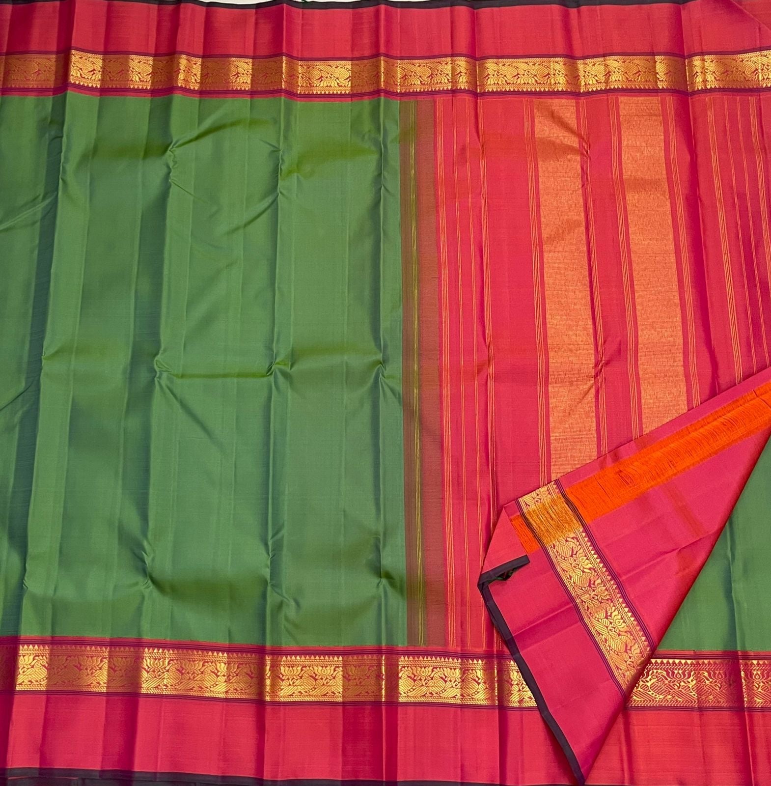 Full view of green saree body with pink border and gold zari woven band, alongside a pink striped pallu section.