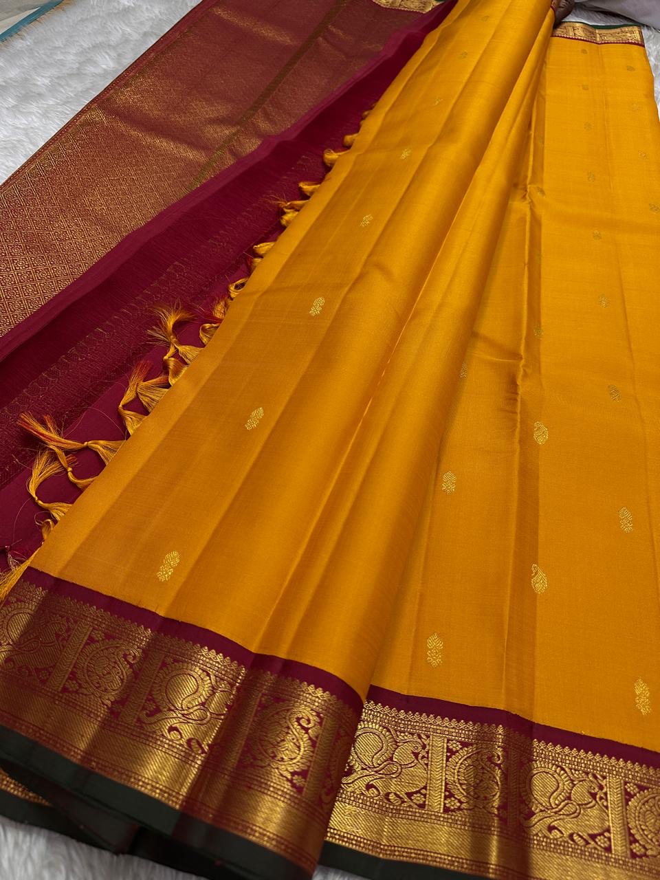 Saffron Royale – Pure Kanchipuram Silk Saree with Peacock Motif Border
Majestic saffron body with delicate zari buttas.
Rich maroon border woven with grand peacock motifs in  zari.
Traditional maroon pallu. Silk Mark Certified, delivery in 2 weeks