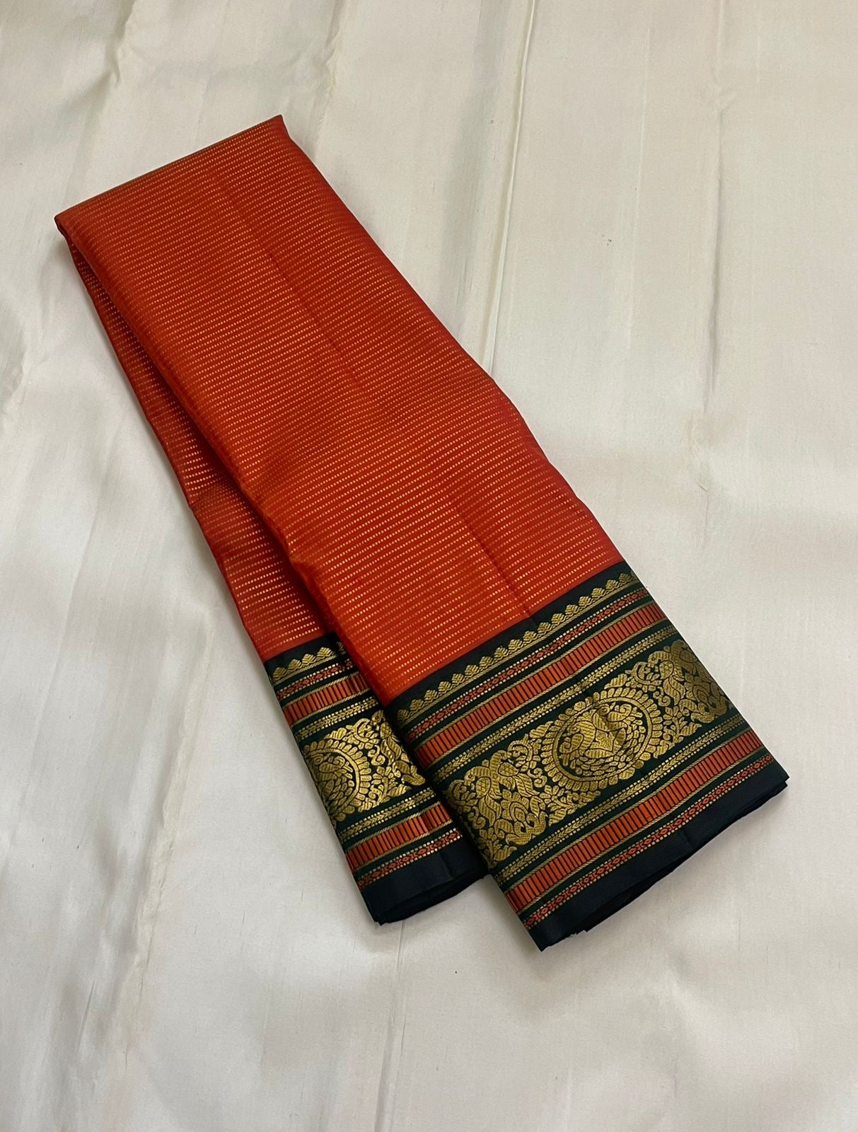 Aruna Mayil Chakram
Pure Kanchipuram Silk Saree – Reddish-Orange Body with Gold Zari Chakram Buttas
Contrast Bottle Green Korvai Borders with Mayil & Temple Motifs
Grand Zari Pallu with Diamond Brocade Weave & Hand-Knotted Tassels
Silk Mark Certified ✅ |
