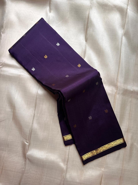 Partly opened purple Kanchipuram silk saree with scattered gold and silver buttas and minimal gold zari border on an ivory silk base.