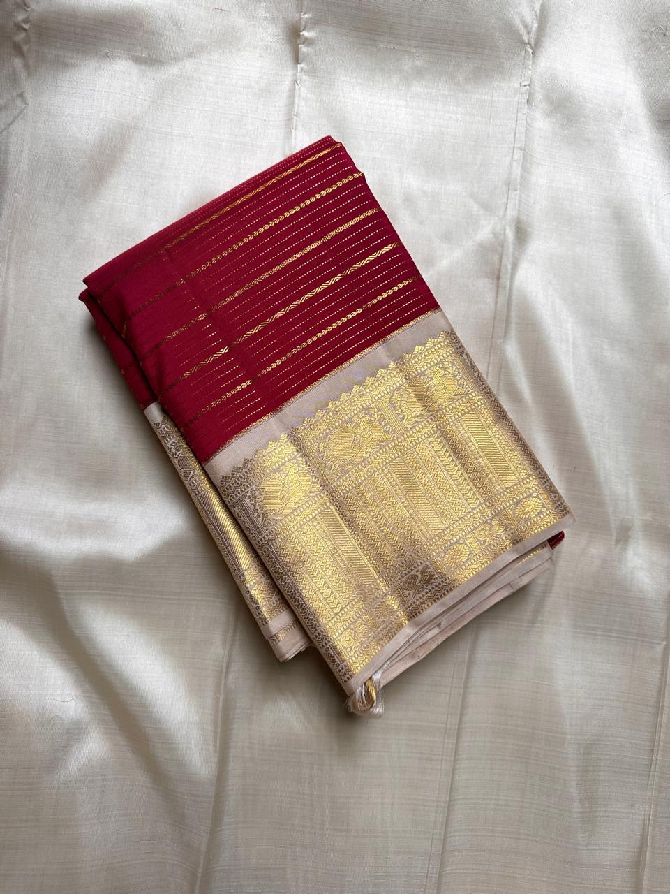 Folded ivory and red Kanchipuram silk saree with gold temple zari border on a cream backdrop