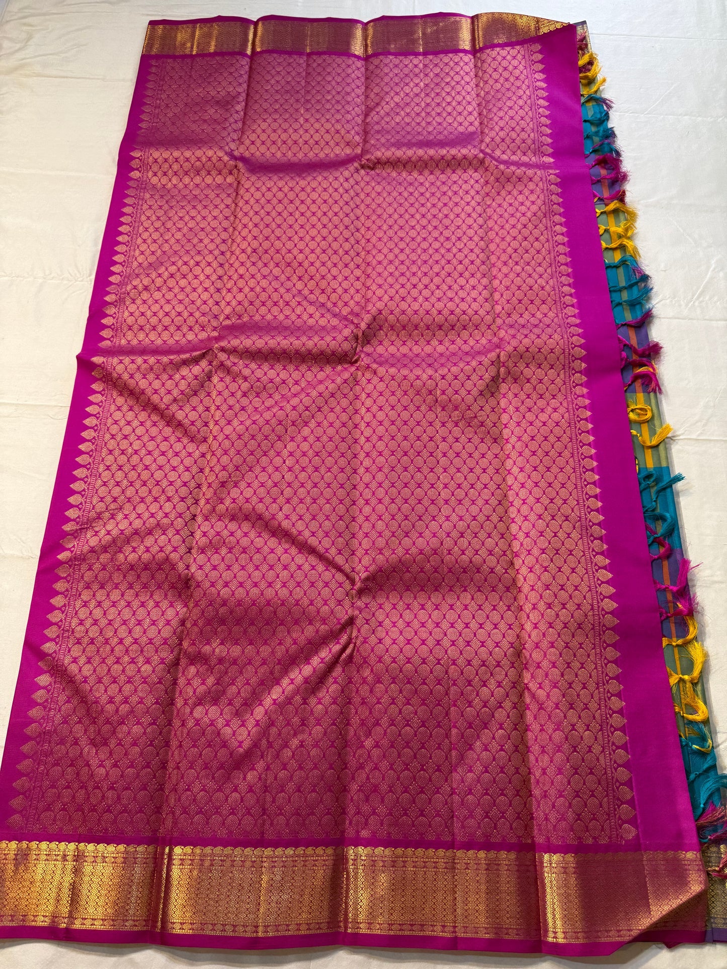 Rangoli Kattam – Pure Silk Kanchipuram Saree
Vibrant multicolor kattam checks with golden zari buttas across the body
Rich rani pink pallu with intricate zari weaving for a grand finish
Contrast purple borders edged with gleaming zari motifs