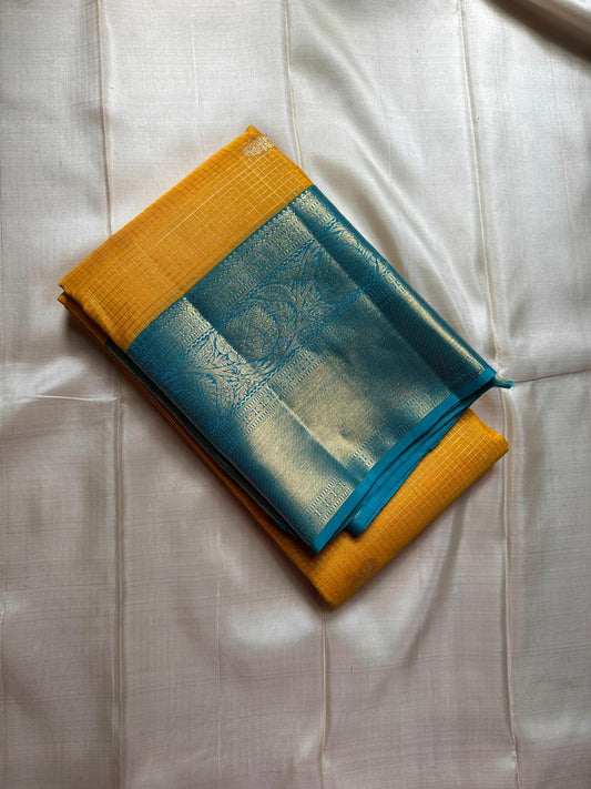 This radiant yellow pure silk drape is elevated by an exquisite and unexpected pairing — a serene sky blue border, making it both eye-catching and rare. Fine zari checks shimmer gently across the body, timeless bavaanji border