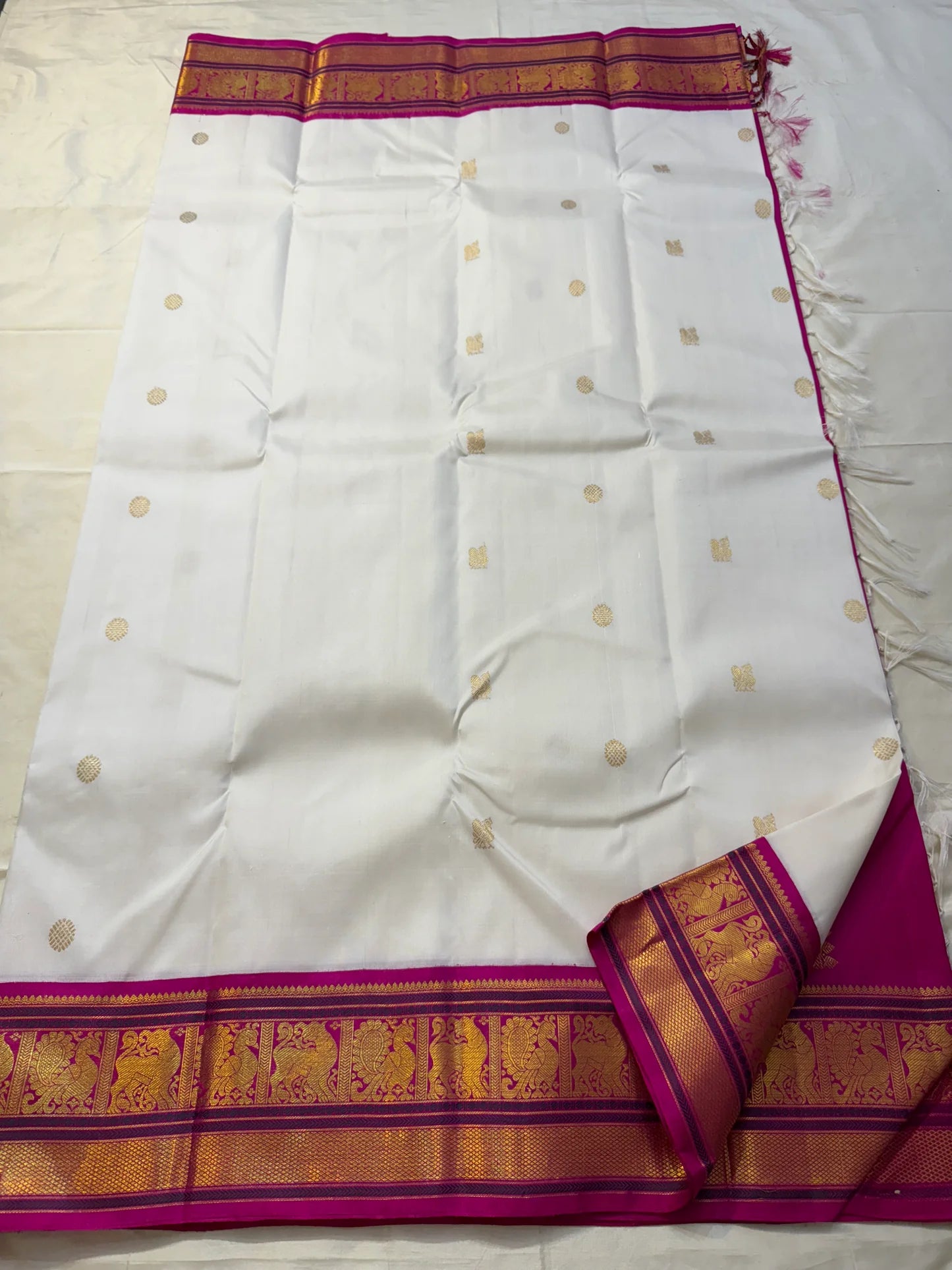 Full-length ivory silk saree with scattered gold buttas, fuchsia zari border, and tassels along the edge