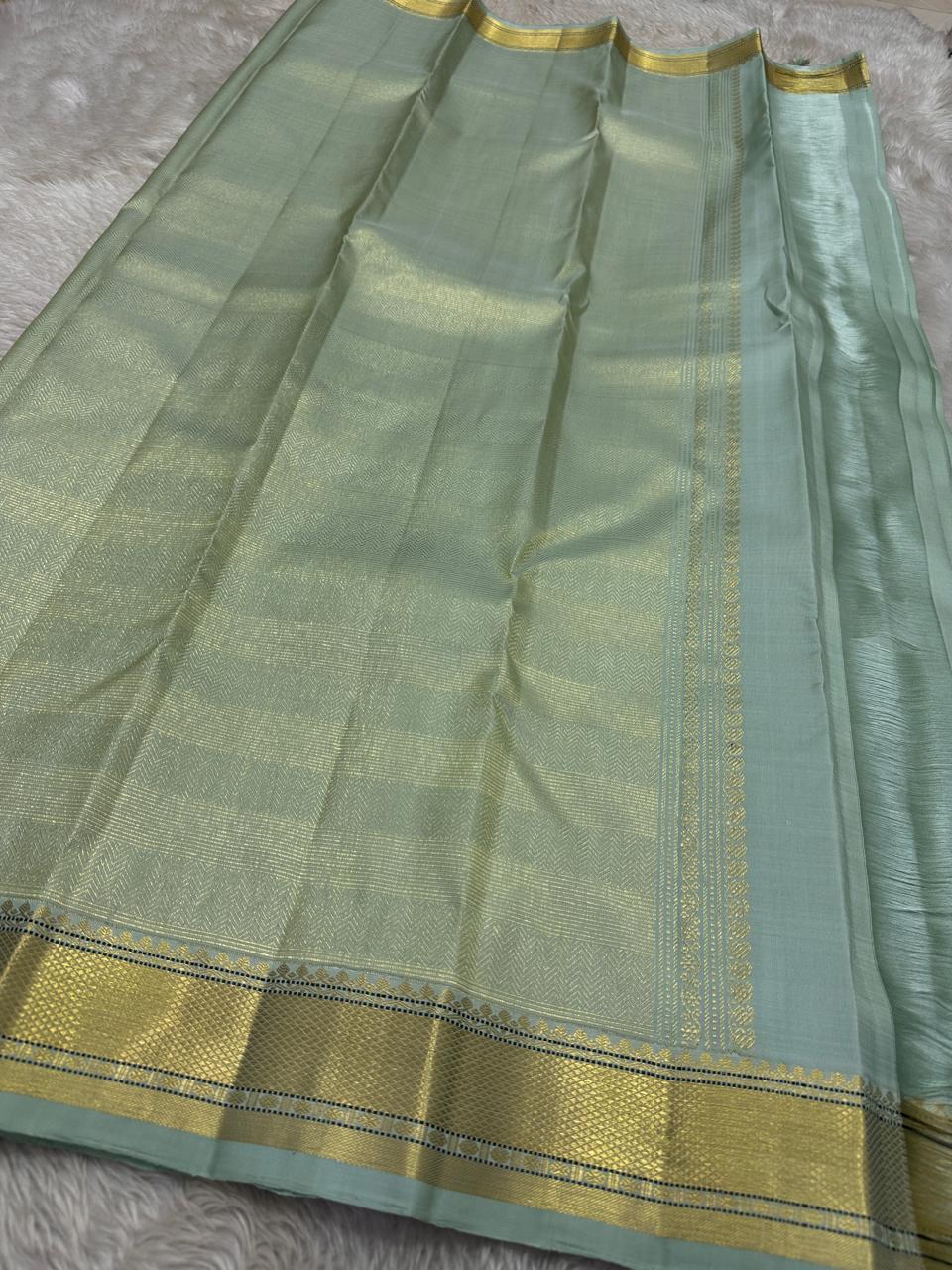 Mint Kattam – Pure Kanchipuram Silk Saree
Pastel Mint Green Body with Fine Zari Checks & Buttas
Broad Gold Zari Border with Textured Tissue Weave
Rich Gold Zari Pallu in Chevron & Striped Bands

Silk Mark Certified, delivery in 2 weeks